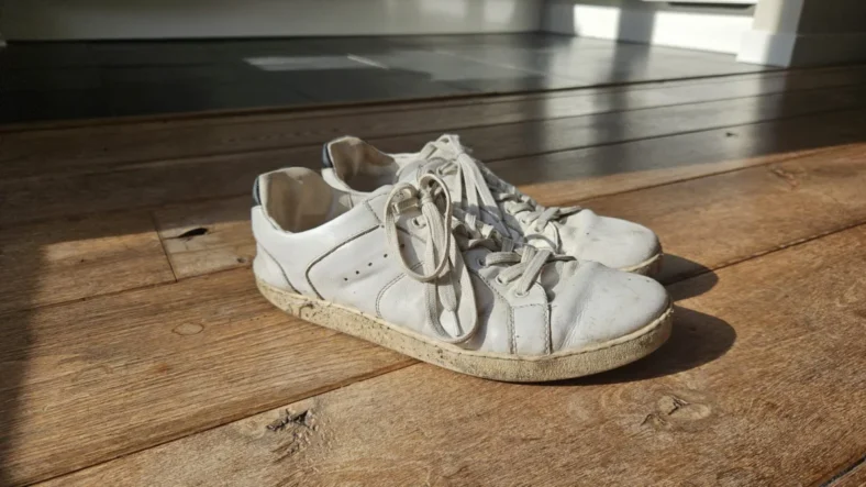 Flink gedragen witte Groundies barefoot sneakers op een houten vloer