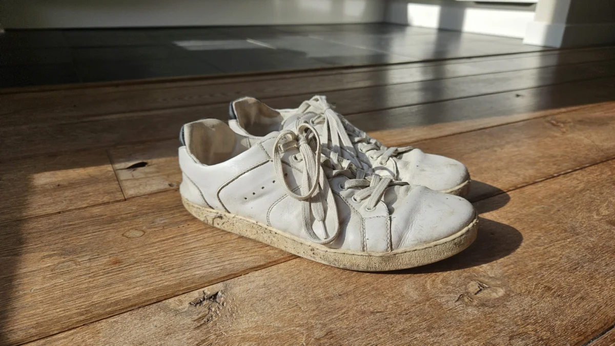 Flink gedragen witte Groundies barefoot sneakers op een houten vloer